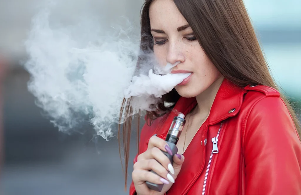 vape store Mckinley - young woman in red jacket exhaling large vapor cloud from vape