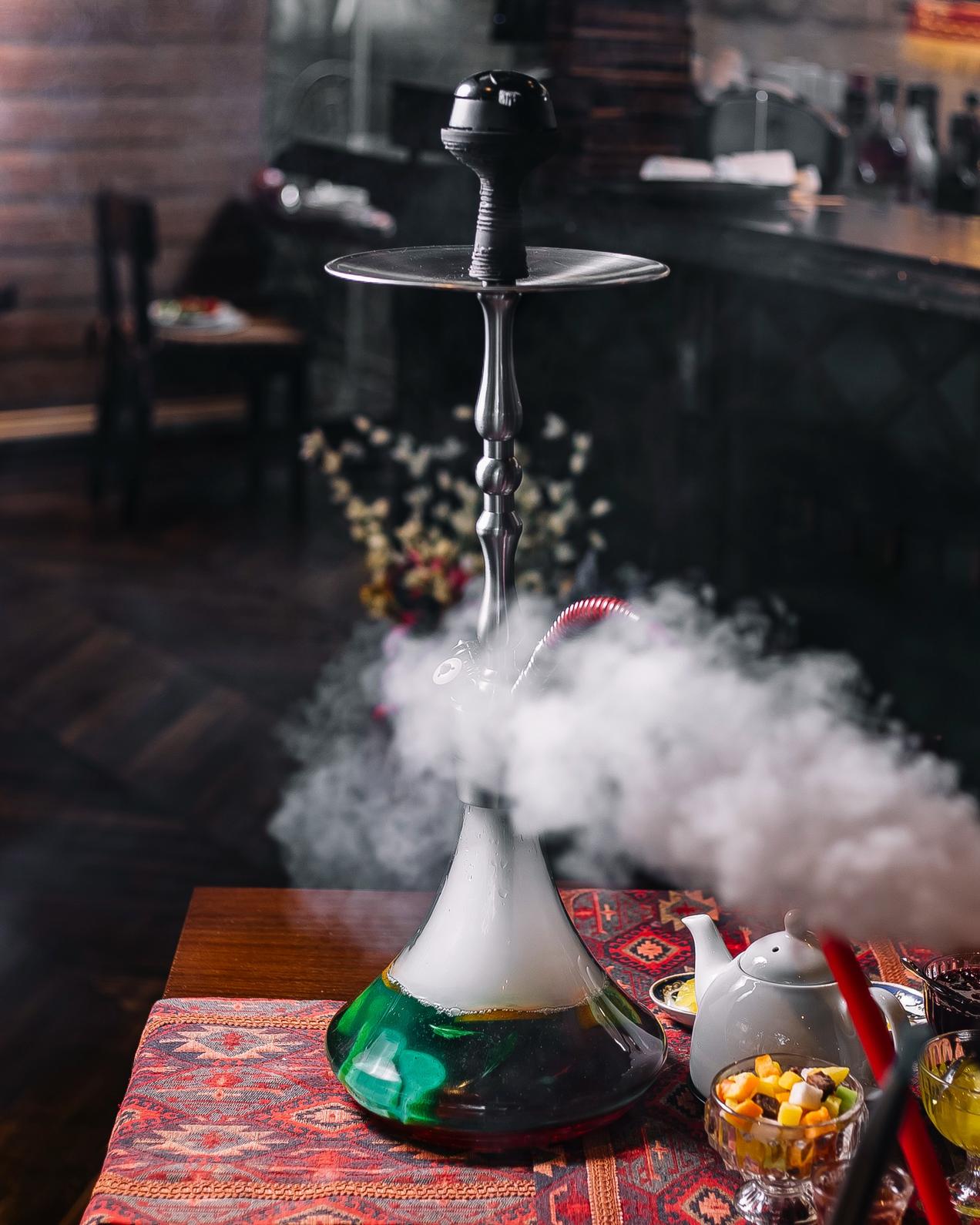 A colorful hookah emitting smoke on a table with tea, available at a hookah shop in Broken Arrow.