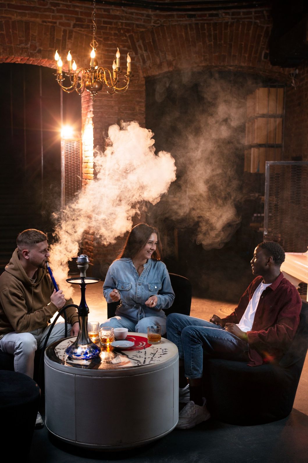 Friends enjoying a hookah session with smoke in a cozy lounge, available at a hookah shop in Broken Arrow.