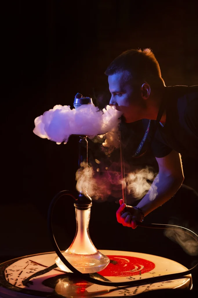 Man smoking hookah with thick clouds in a vibrant Hookah Shop Houston setting with warm lighting.