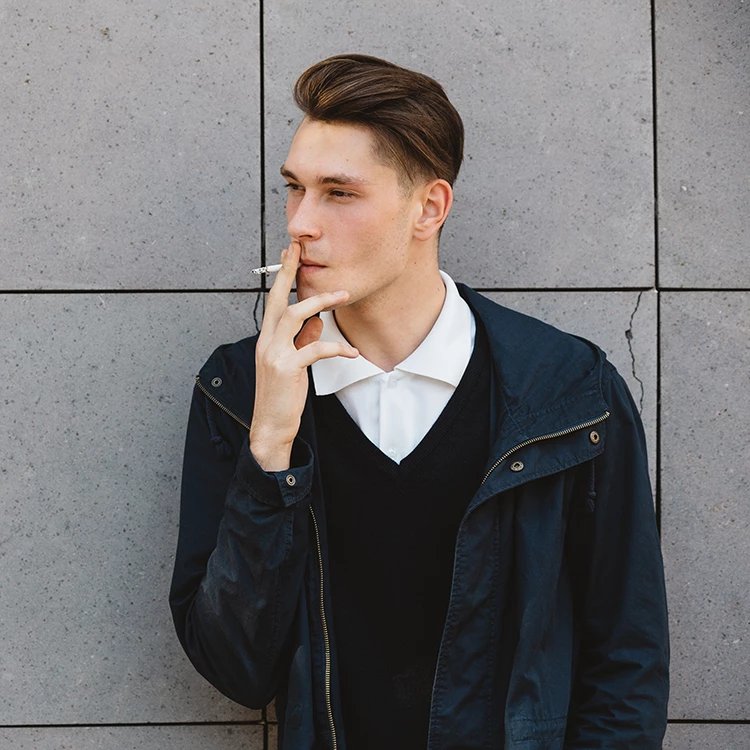 Young man smoking a cigarette against a concrete wall, styled for a Vape Shop Houston blog promotion.