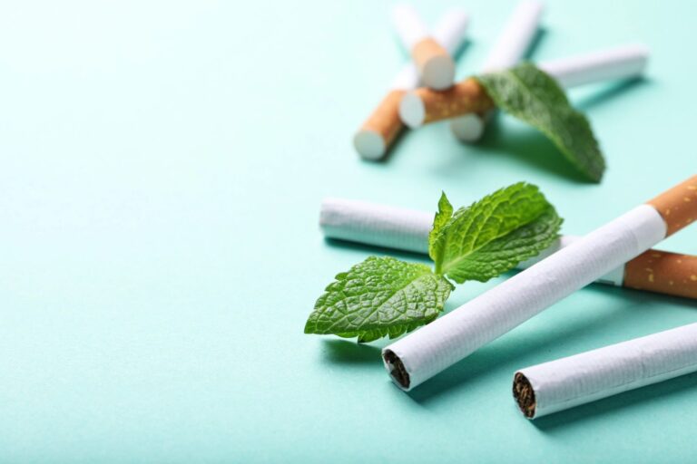 Cigarettes interspersed with fresh mint leaves on a light blue background, featuring menthol varieties at a cigar shop in Broken Arrow.