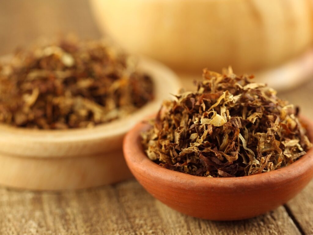 Close-up of premium, hand-picked tobacco leaves in a rustic wooden bowl, showcasing rich brown and golden hues, available at Tobacco Shop Houston.
