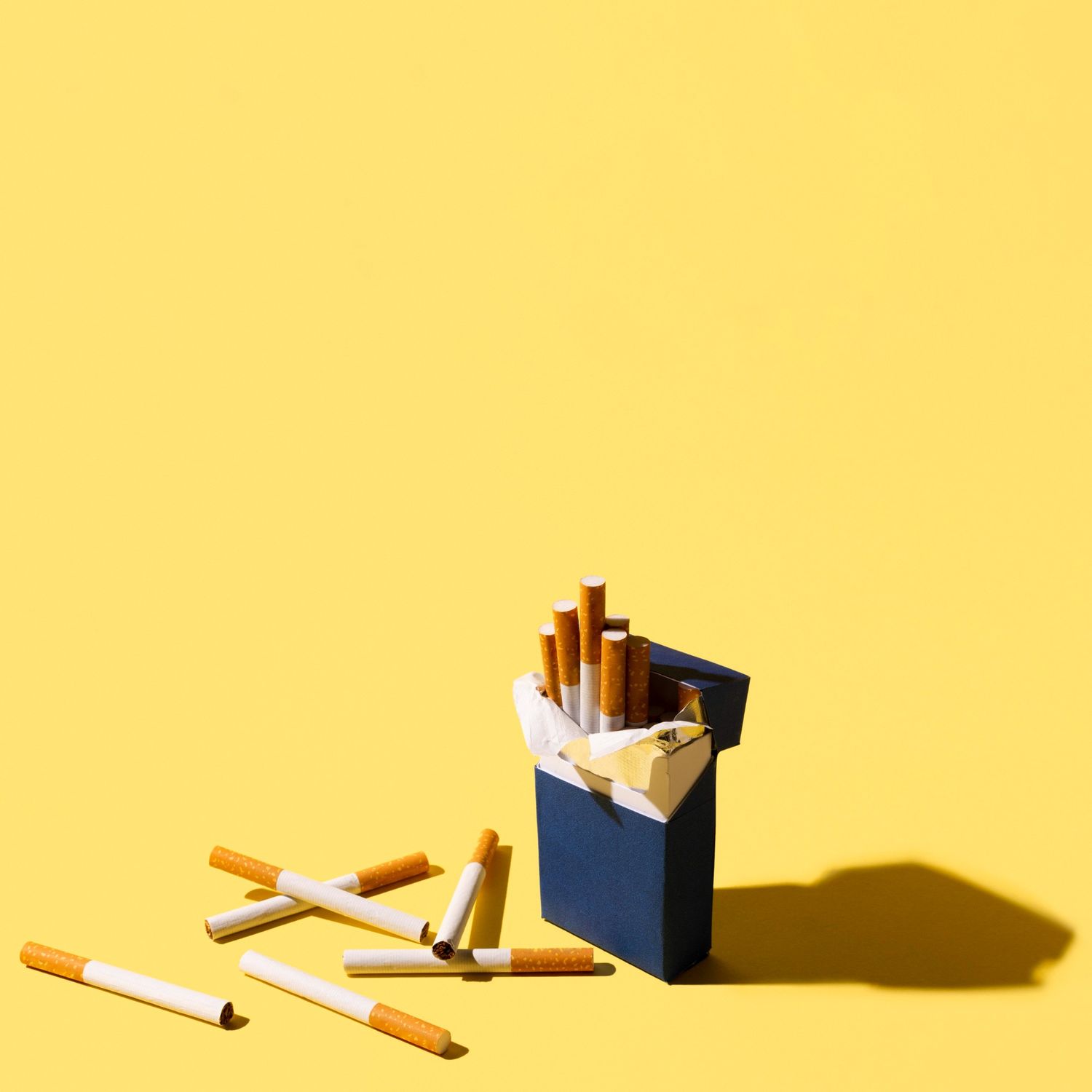 Open blue cigarette pack with scattered cigarettes on a bright yellow background, available at a cigar shop in Broken Arrow.
