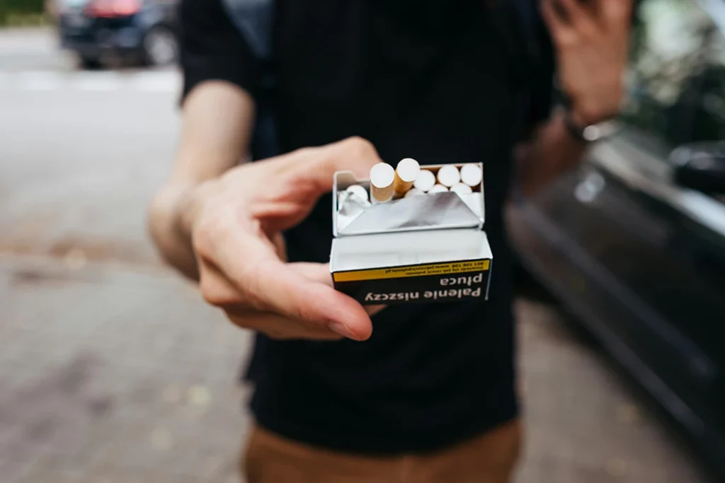 Person holding an open pack of cigarettes near Cigarette Shop Tulsa, with a blurred street background.