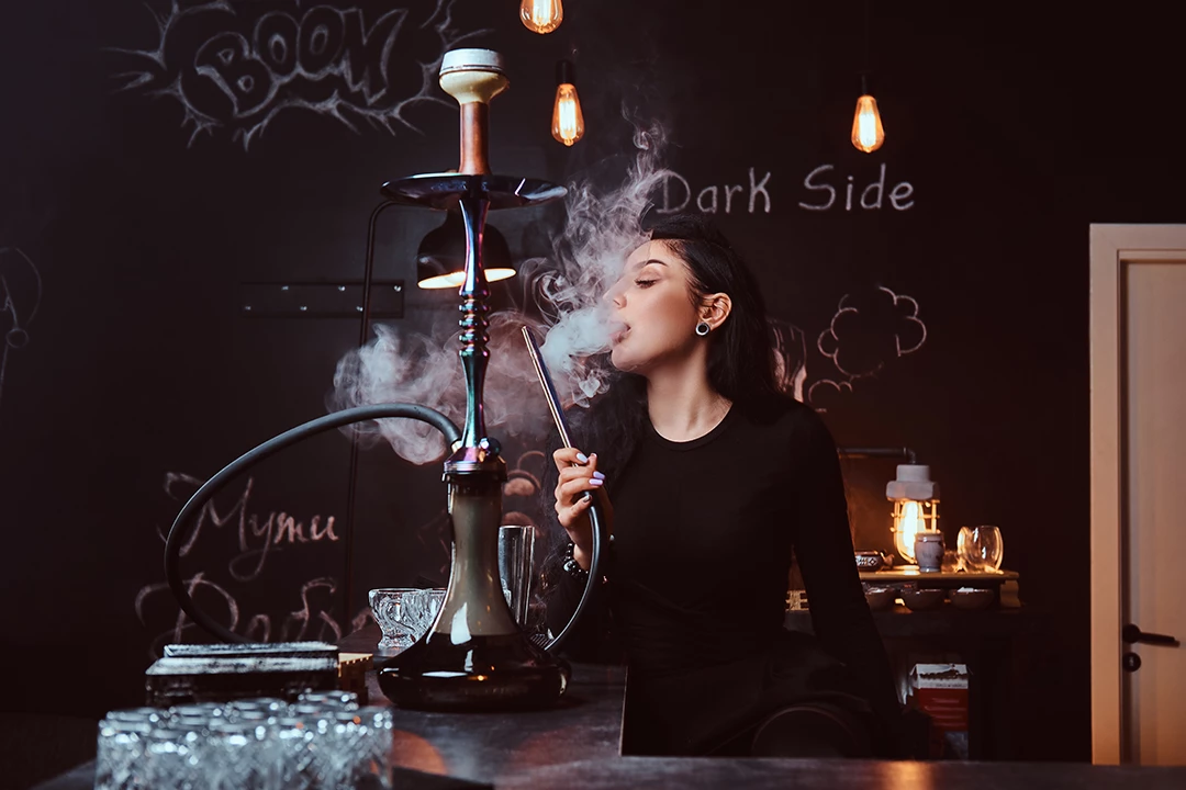 Woman enjoying hookah in atmospheric Hookah Shop Houston lounge with graffiti walls and dim Edison lights.