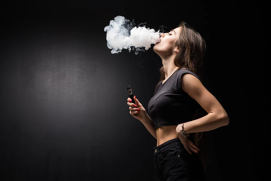 Woman vaping with thick clouds against a dark background, highlighting a sleek Vape Shop Houston style