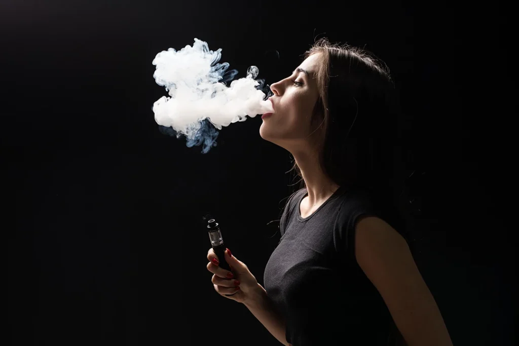 Woman vaping with thick clouds against a dark background, promoting a stylish Vape Shop Houston experience.
