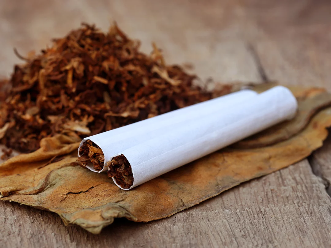 Hand-rolled cigarettes with tobacco on a tobacco leaf, displayed by a tobacco store Houston on a wooden surface.