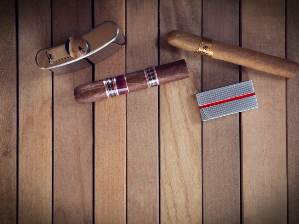 Premium cigars and smoking accessories displayed at Head Shop Houston, featuring a stylish silver cigar lighter with a classic design, placed on a warm wooden table alongside a finely crafted cigar with colorful bands.