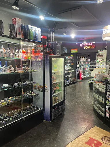 Shelves of glass pipes and a fridge with drinks in a head shop in Houston, with “accessories, vaporizers, hookahs, kratom" displays.