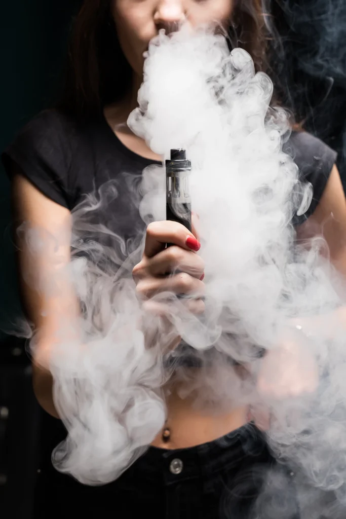 Woman vaping with thick clouds, showcasing a stylish Vape Shop Houston experience against a dark backdrop.