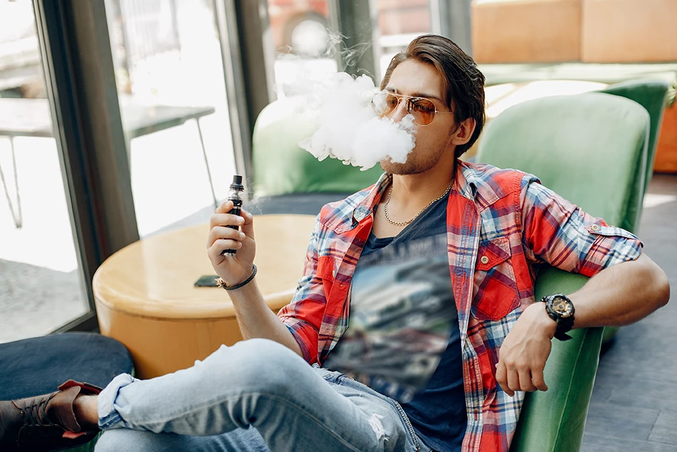 Man vaping in a modern Vape Shop Houston lounge with green chairs and large windows, enjoying a relaxed vibe.