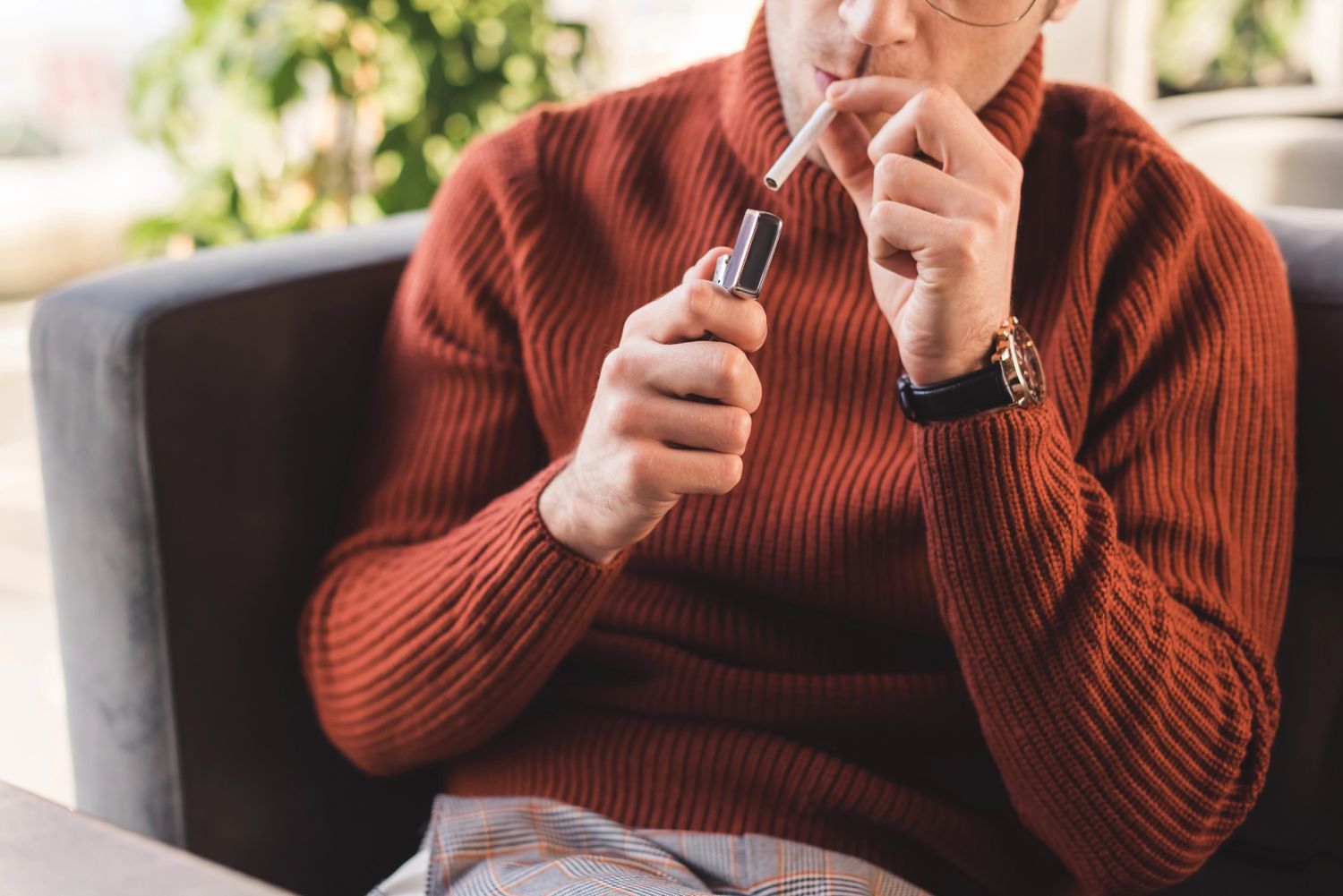 A man lighting a cigarette with a lighter, styled in a cozy setting from Vape Shop Houston.