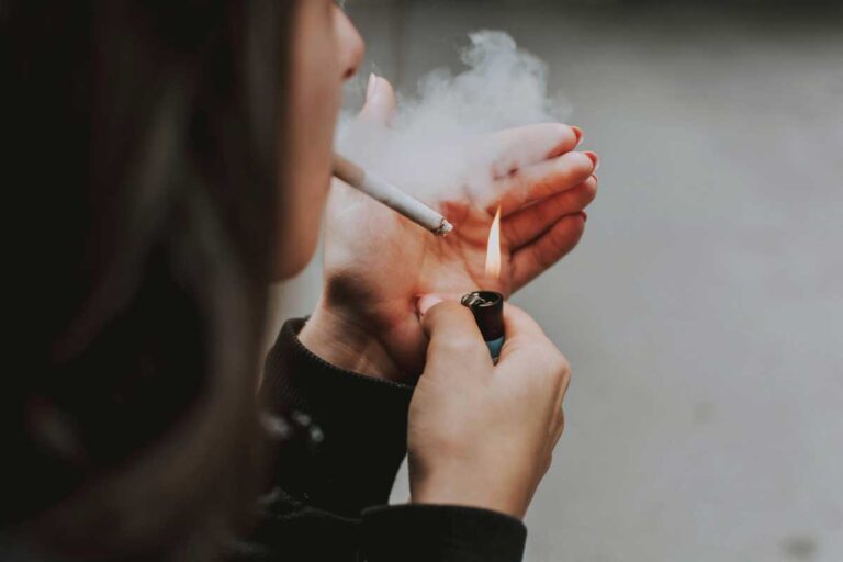 Woman lights a cigarette, smoke billows up, showing lighters and tobacco products available at smoke shop broken arrow.