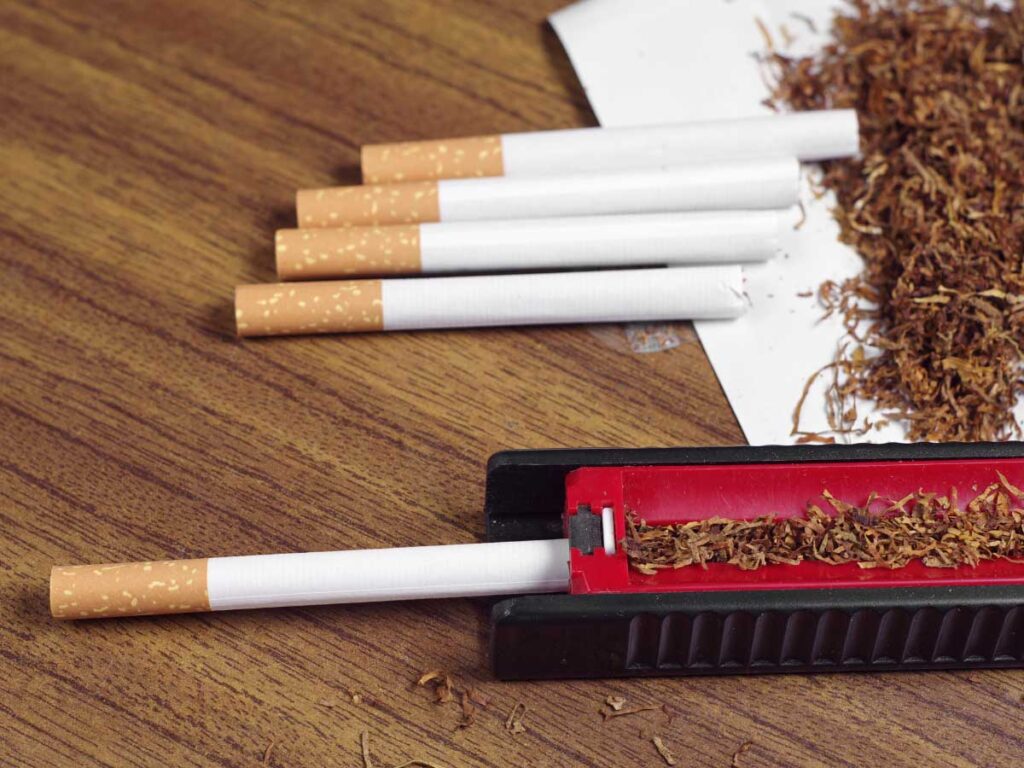 Assorted cigarettes and fresh loose tobacco displayed on a wooden surface near a rolling machine at our Broken Arrow tobacco store, ideal for custom roll-your-own enthusiasts.