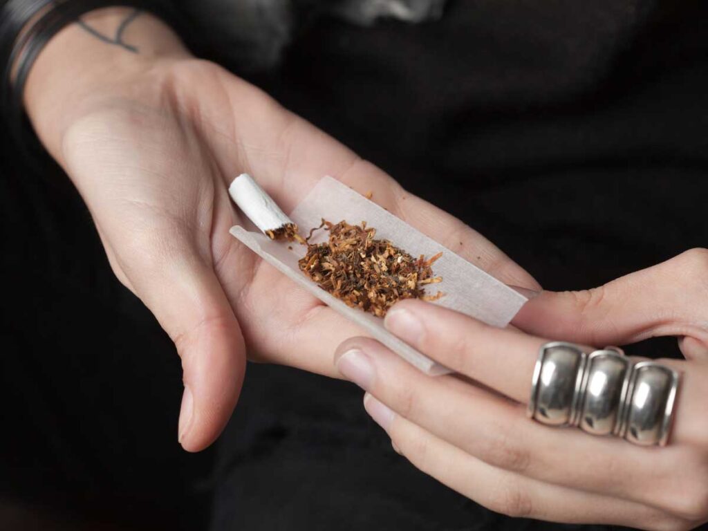 Hands expertly rolling a cigarette with high-quality tobacco on thin paper, available at the leading tobacco store in Broken Arrow for personalized smoking experiences.