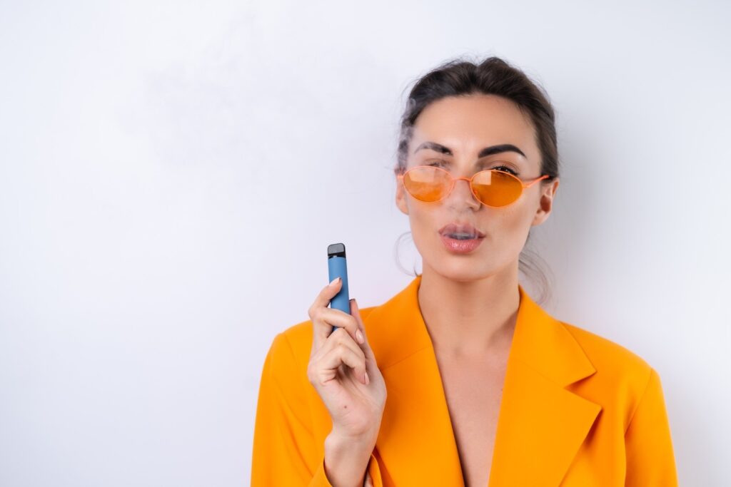 Confident woman in orange blazer holding vape supplies in Houston, promoting modern vaping trends.
