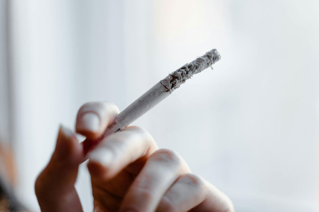 Close-up of a hand holding a lit cigarette with a long ash, get fresh products and accessories at a smoke shop broken arrow.
