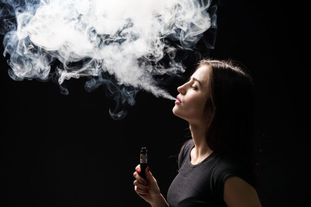 Woman in black exhaling vapor with vape supplies in Houston, highlighting sleek vaping style.
