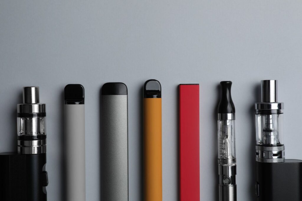 Assorted stylish vape devices lined up against a gray backdrop at a top vape store in Houston for enthusiasts.