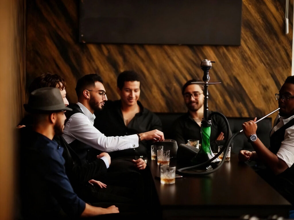Diverse group of men relaxing with drinks at a stylish hookah shop in Tulsa, savoring smooth flavors in a warm wooden lounge setting.