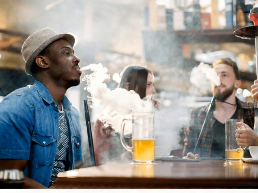 Friends exhaling flavorful smoke while chilling at a trendy hookah shop in Tulsa, creating a relaxed and smoky outdoor vibe.