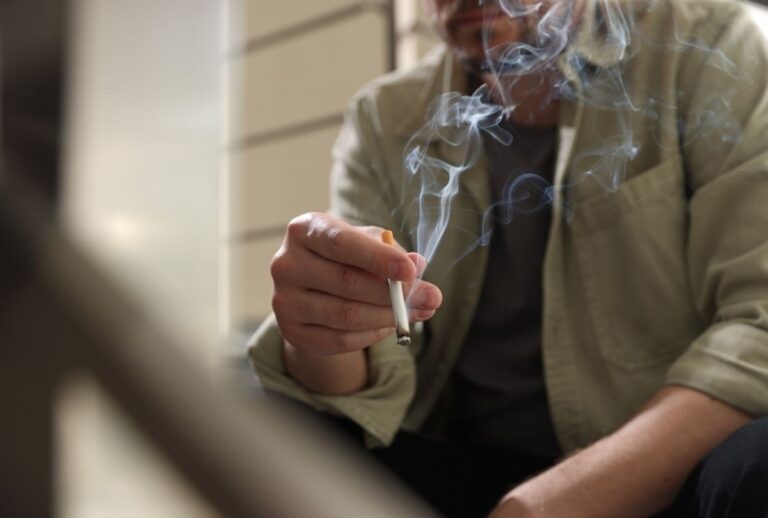 Smoker holding lit cigarette with rising smoke, promoted by cigarette shop Tulsa for classic tobacco product visibility.