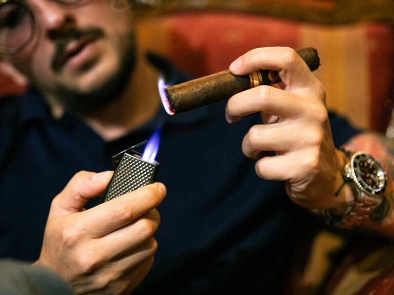 Man lighting a premium cigar at a cozy tobacco shop in Broken Arrow, showcasing a stylish smoking experience with a sleek lighter.