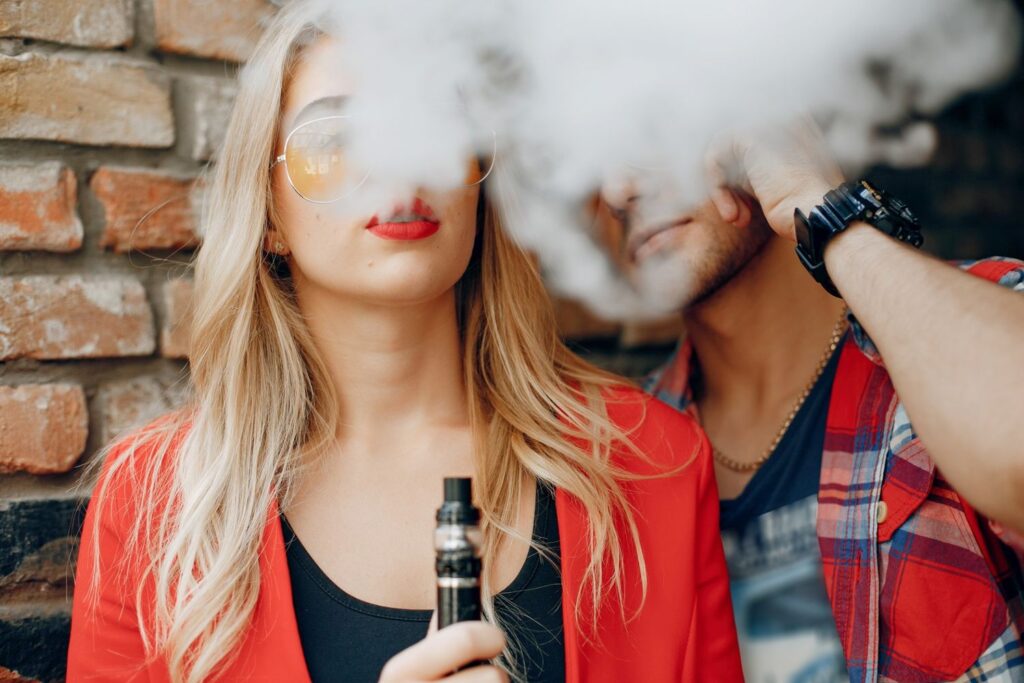 Stylish couple enjoying vape supplies in Houston against a brick wall, showcasing trendy vaping culture.