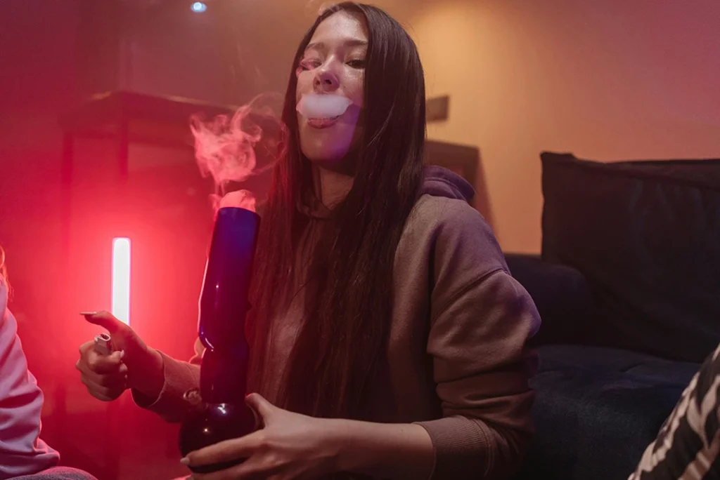 Young woman exhaling smoke while using a water pipe in moody red-lit room, candid portrait — cigarette shop Tulsa vibe
