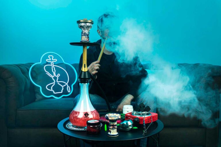 Man exhales smoke from a modern hookah under blue neon lighting, selling accessories at your nearby hookah shop broken arrow.