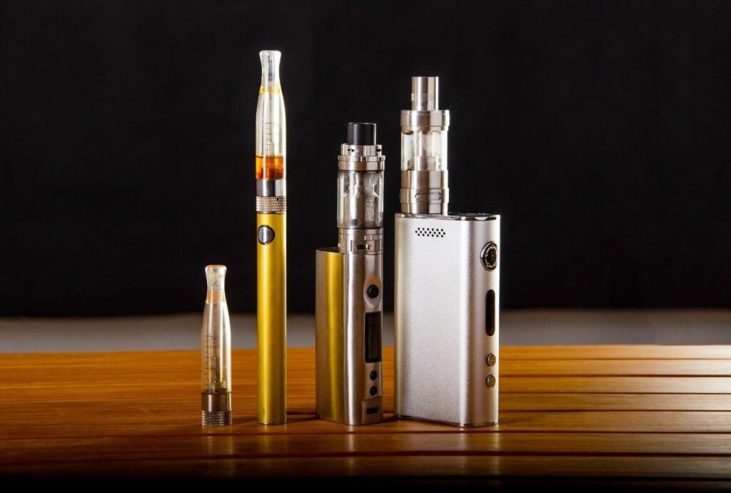 Assorted vape pens and mods displayed on wood table at cigarette shop Tulsa offering smoking alternatives and accessories.