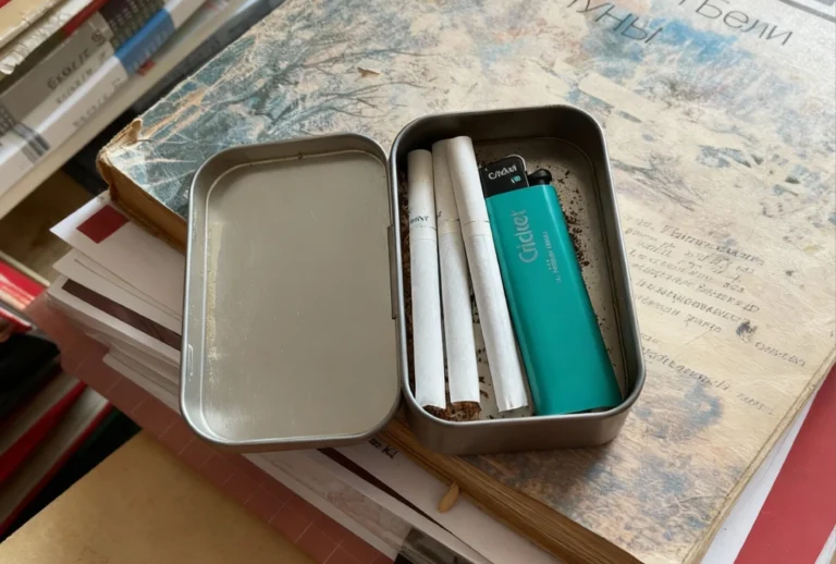 Portable tin with cigarettes, teal Cricket lighter, and tobacco on vintage book at CBD Shop Tulsa.