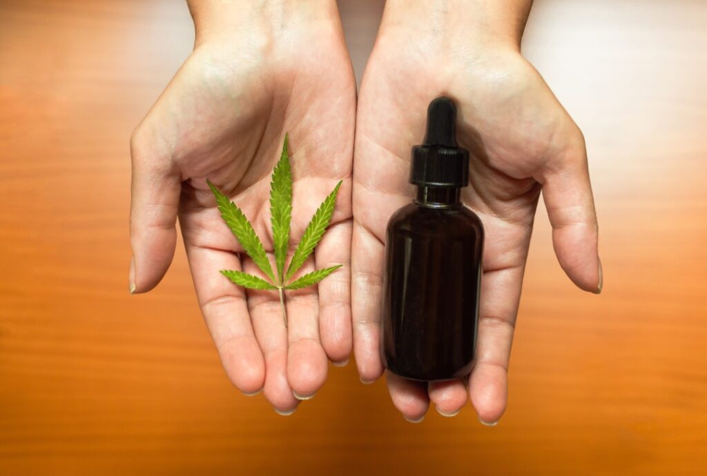 Hands holding a CBD oil bottle and hemp leaf available at your local CBD Shop Tulsa.
