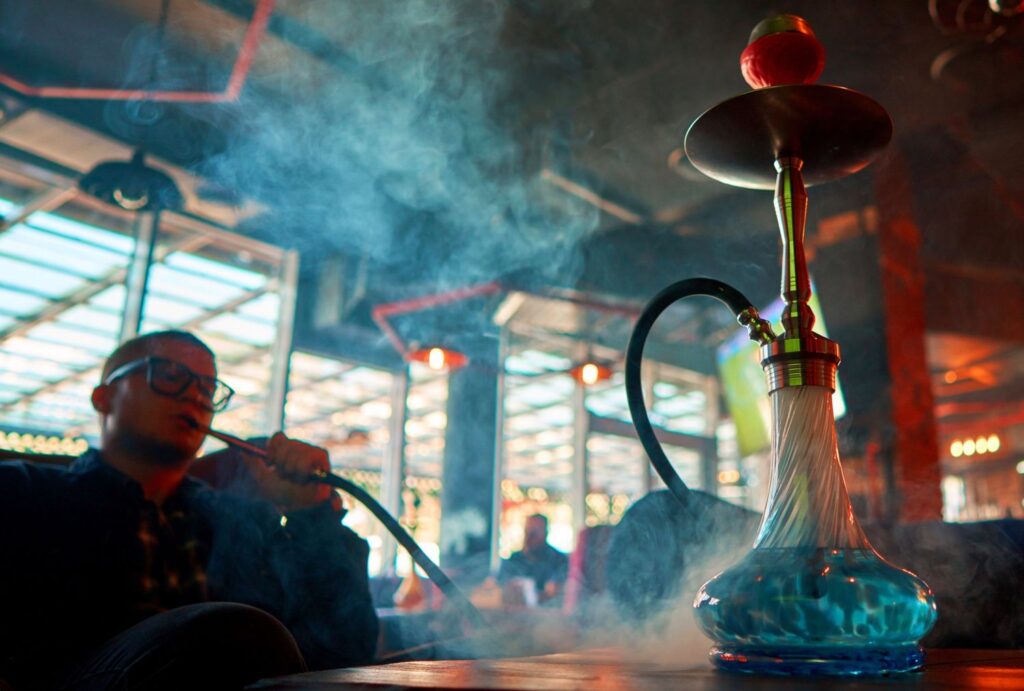 Man smoking hookah with blue water base in modern lounge, featured in smoke shop Tulsa ad for premium shisha accessories