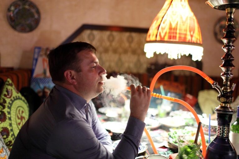 Man enjoying hookah in decorated lounge with orange hose, promoted by smoke shop Tulsa for cultural smoking experiences.