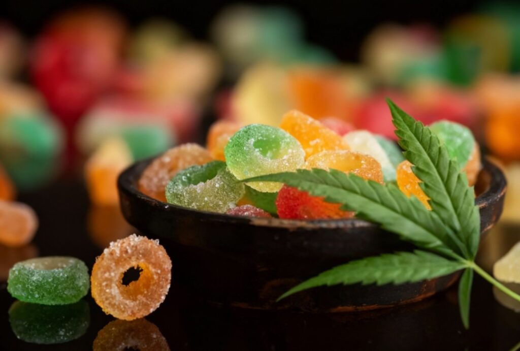 Vibrant CBD gummies with cannabis leaf in bowl at CBD Shop Owasso, showcasing delicious hemp-infused options nearby.