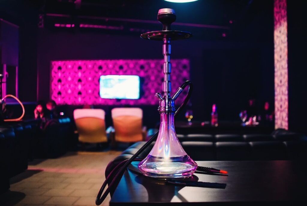 Glass hookah on a table in a dark, neon pink lounge. Visit the best Head Shop Houston for supplies.