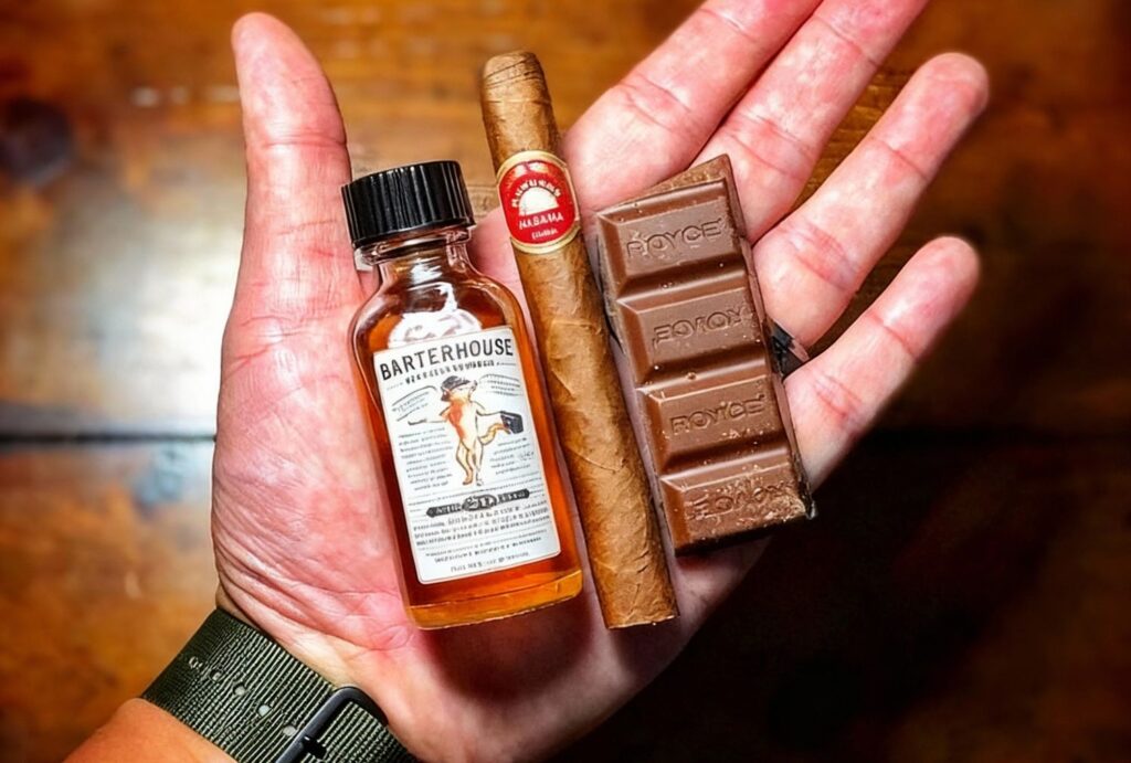 Hand holding Barterhouse whiskey, premium cigar, and Royce chocolate at Cigar Shop Sapulpa lounge.