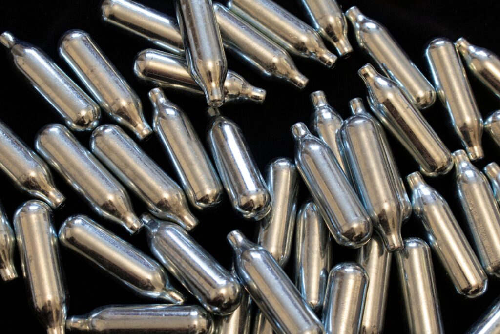 Close up view of shiny silver nitrous oxide Owasso chargers scattered on a dark black background for food service.