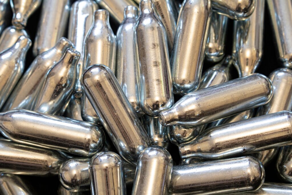 Close up texture of bulk silver nitrous oxide Owasso whip cream chargers piled together for catering supply use.