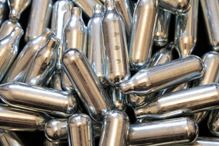 Close up texture of bulk silver nitrous oxide Owasso whip cream chargers piled together for catering supply use.