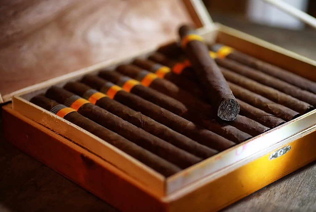 Open wooden box featuring dark, rich-wrapper cigars with orange bands; available at your local cigar shop owasso.