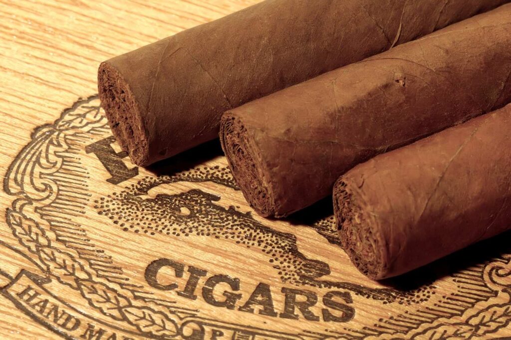 Three hand-rolled brown cigars resting on a carved wooden sign at a top-rated cigar store Owasso.