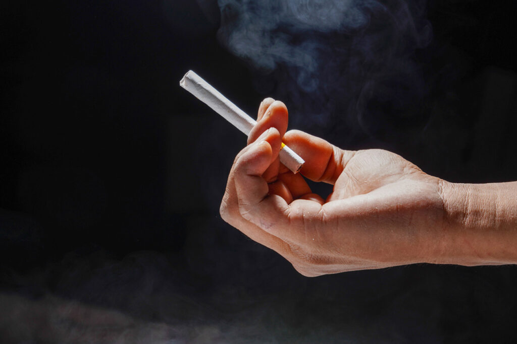 Close-up of hand holding a lit cigarette with rising smoke, highlighting quality smoking experience from Broken Arrow's top cigarette shop.