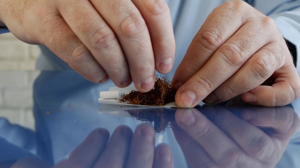 Close-up of hands carefully placing tobacco onto rolling paper with empty filters nearby, quality products available at head shop Sapulpa.