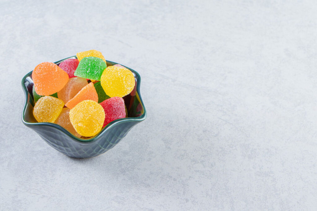 Colorful sugar-coated Delta 8 gummies in green ceramic bowl at top Delta 8 store Broken Arrow.