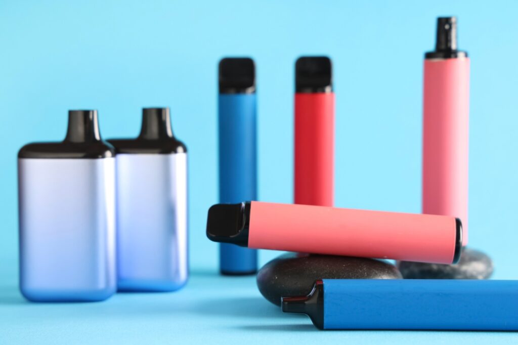 Assortment of cylindrical and box-style disposable vapes in blue and red from a cigar store in Owasso, Oklahoma.