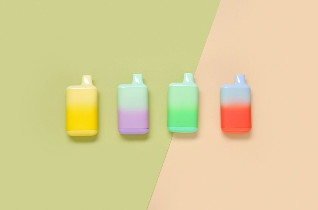 Four gradient pastel-colored disposable vapes displayed on a split background, available at a cigar store in Owasso.